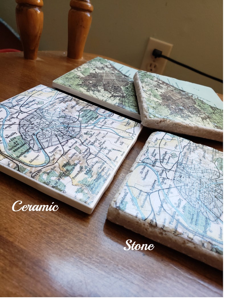May include: Three square coasters featuring vintage map prints of Paris and its surrounding suburbs. One coaster is smooth white ceramic, while the other two have a textured, porous stone edge. The maps display street grids, rivers, and city names.