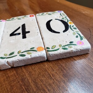 May include: Three white ceramic tiles with black numbers 40 painted on them. Each tile has a green leafy design with small pink, orange, and purple flowers.