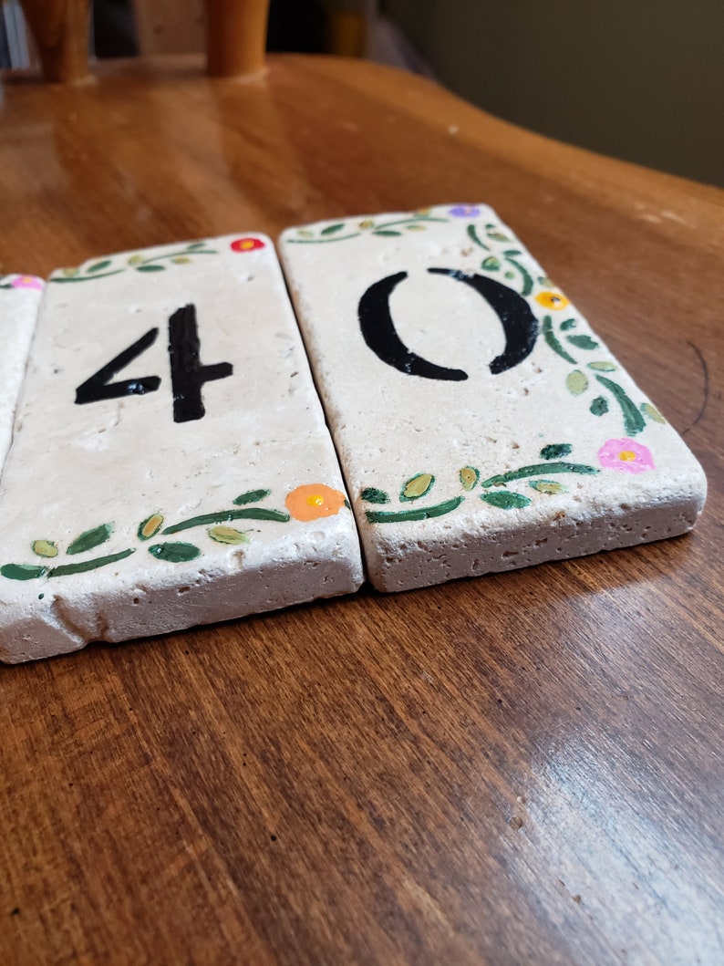 May include: Three white ceramic tiles with black numbers 40 painted on them. Each tile has a green leafy design with small pink, orange, and purple flowers.
