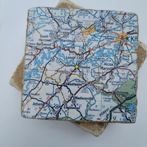 May include: A square stone coaster featuring a printed road map of the Loudon, Tennessee area. The map displays various highways, town names like Oak Ridge and Maryville, and a yellow star marking the location of Loudon on a textured surface.