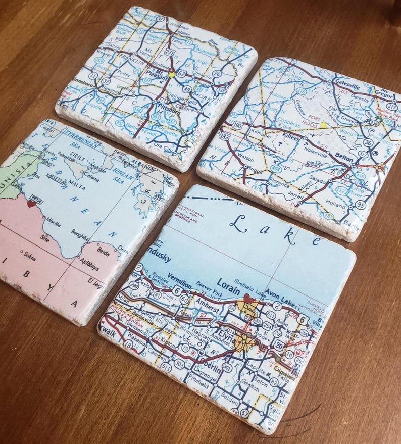 May include: Four square stone coasters featuring printed map sections. One shows the Mediterranean Sea, another displays the Lake Erie region, and two depict various highway and road networks with labelled towns and cities in blue, red, and black ink.