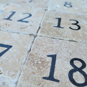 May include: A close-up of a stone patio with numbered tiles. The numbers are in black paint and range from 1 to 18.