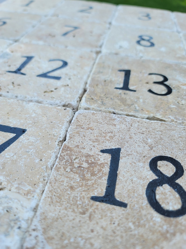 May include: A close-up of a stone patio with numbered tiles. The numbers are in black paint and range from 1 to 18.
