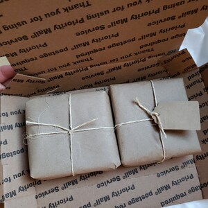 Puede incluir: Dos paquetes peque&ntilde;os y cuadrados envueltos en papel marr&oacute;n y atados con hilo, dentro de una caja de cart&oacute;n. Un paquete tiene una etiqueta peque&ntilde;a adjunta. La caja est&aacute; impresa con "Priority Mail" y "Thank you for using Priority Mail Service".
