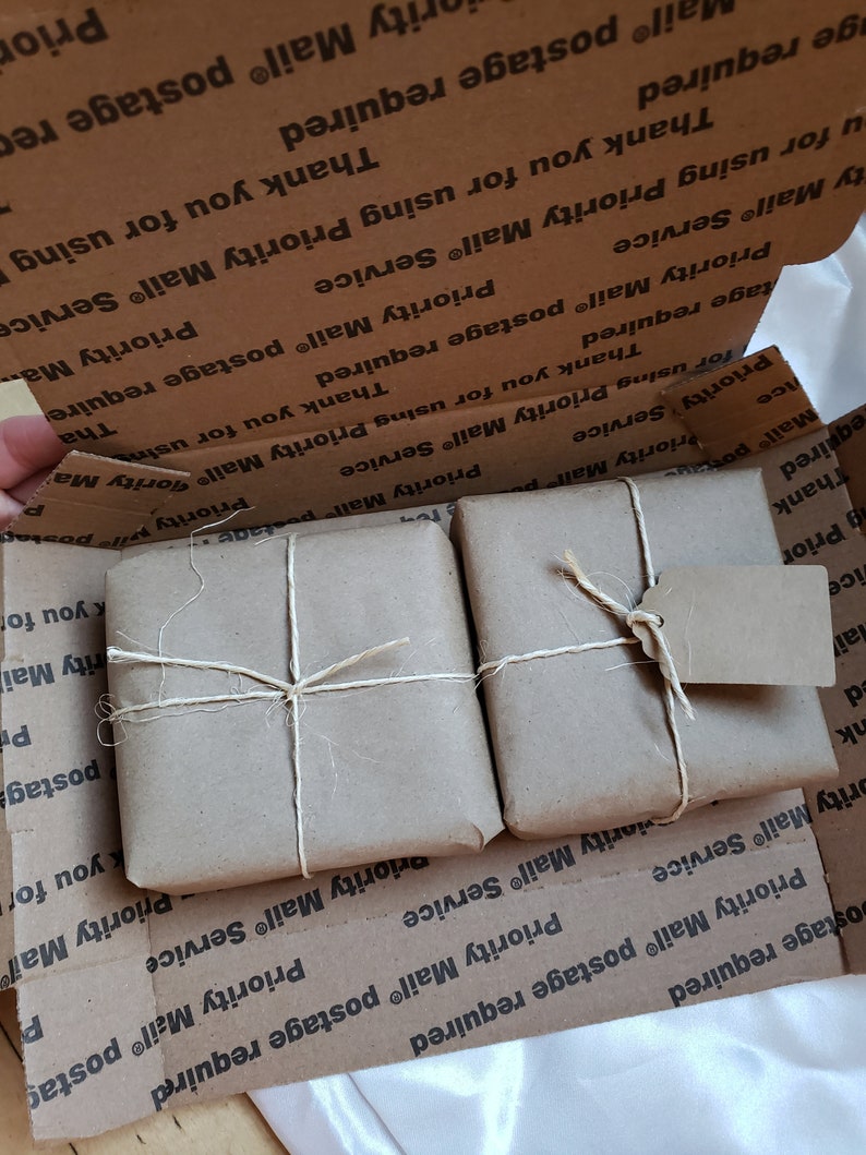 Puede incluir: Dos paquetes peque&ntilde;os y cuadrados envueltos en papel marr&oacute;n y atados con hilo, dentro de una caja de cart&oacute;n. Un paquete tiene una etiqueta peque&ntilde;a adjunta. La caja est&aacute; impresa con "Priority Mail" y "Thank you for using Priority Mail Service".