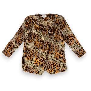 May include: A long-sleeved top with a leopard print pattern in shades of brown, tan, and black. The top has a V-neckline and a button closure. The garment is made of a lightweight fabric.