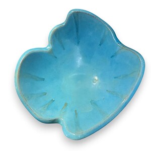 May include: A bright turquoise ceramic bowl with an irregular, organic shape resembling a leaf. The bowl features a smooth, glossy glaze with subtle variations in color intensity and defined ridges radiating from the center to the scalloped edges.