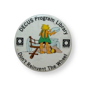 May include: A round white pinback button featuring a cartoon of a caveperson with yellow hair and a green tunic pushing a wooden cart with stone wheels. The text reads DECUS Program Library and Don't Reinvent The Wheel with two DECUS logos.