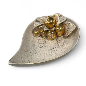 May include: A leaf-shaped ceramic dish with a speckled, off-white surface and gold trim. The dish is decorated with gold-colored fruit and white leaves with gold accents. Decorative gold swirls are on the dish.