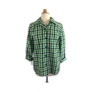 May include: A green, navy, and white plaid button-down shirt. The long-sleeved shirt is displayed on a mannequin. The shirt has a collared neckline and buttons down the front. The sleeves are rolled up.