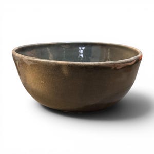 May include: A handmade ceramic bowl with a dark brown exterior and a darker interior. The bowl has a rounded shape with a slightly flared rim. The surface has a textured appearance, and the bowl is sitting on a white surface.
