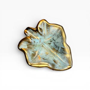 May include: A decorative leaf-shaped dish with a metallic gold rim and a turquoise and gold interior. The dish has a textured surface and is likely made of ceramic or metal. The overall design is organic and artistic.
