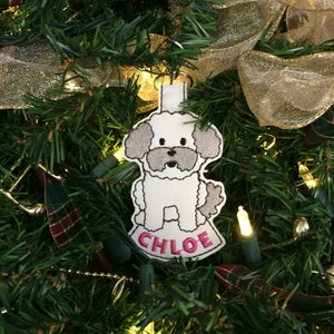 May include: White felt Christmas ornament with a gray embroidered poodle and the name "CHLOE" in pink embroidery.
