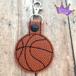 May include: A brown leather basketball keychain with a black stitching detail. The keychain has a silver metal clip.
