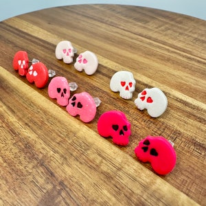 May include: A set of 10 skull-shaped earrings with a heart design. The earrings are made of polymer clay and come in a variety of colors, including white, pink, and red.