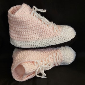 May include: A pair of pink and white crocheted slipper shoes in the shape of high-top sneakers.