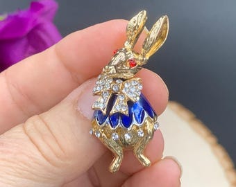 May include: A gold-tone rabbit brooch with blue enamel and rhinestones. The rabbit has red eyes and a white bow.