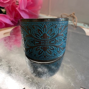 Op de afbeelding: Een brede, zilverkleurige armband met een blauw en bruin bloemenmotief. De armband is gegraveerd met een gedetailleerd patroon.