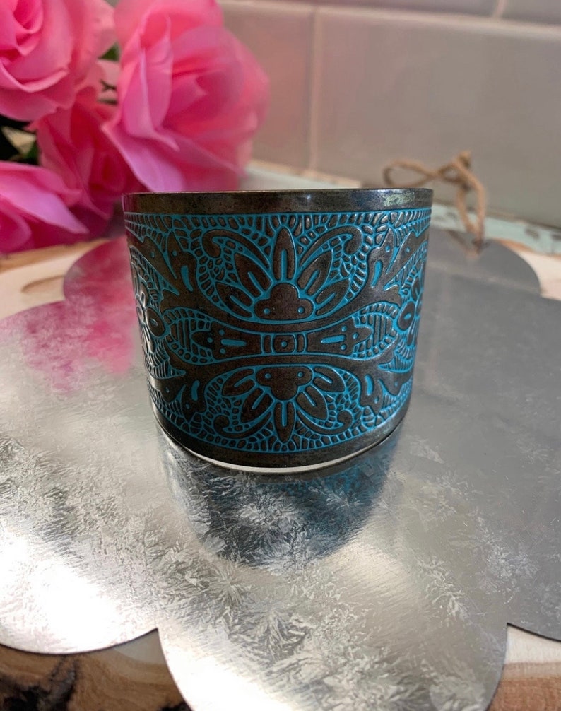 Op de afbeelding: Een brede, zilverkleurige armband met een blauw en bruin bloemenmotief. De armband is gegraveerd met een gedetailleerd patroon.