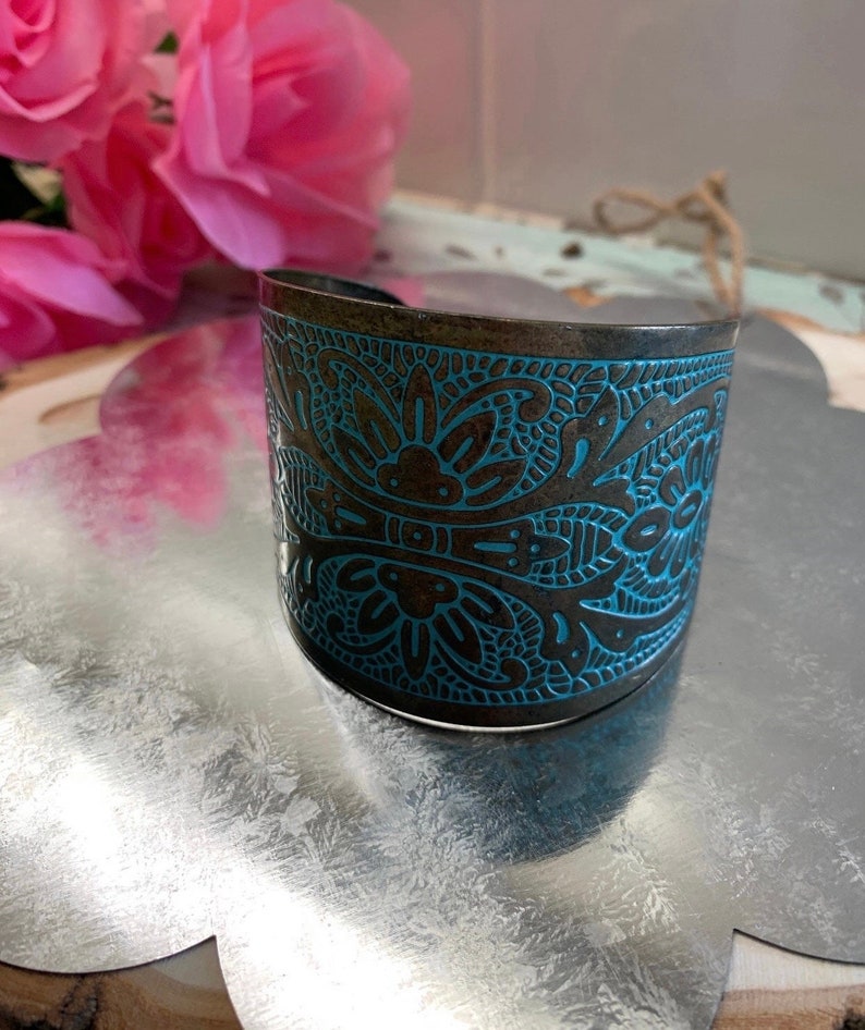 Op de afbeelding: Een brede metalen armband met een ingewikkeld blauw en bruin bloemenmotief. De armband is gemaakt van donker metaal met een licht verweerde afwerking.