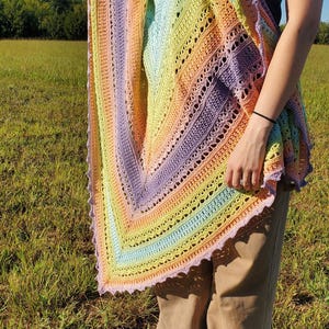 May include: A rainbow crochet shawl with a delicate lace pattern. The shawl is draped over a person's shoulders and is made with a variety of pastel colors.