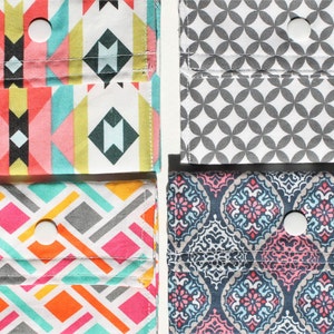 May include: Four fabric pouches with different patterns, each with a buttonhole and a white button. The pouches are arranged in two rows of two. The top row features a geometric pattern in pink, blue, and yellow, and a gray and white pattern. The bottom row features a geometric pattern in pink, blue, and orange, and a blue and pink pattern.