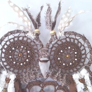 May include: A brown crocheted owl dreamcatcher with white feathers and beads. The owl's eyes are made of brown crocheted circles with white beads. The owl's beak is made of a white stone.