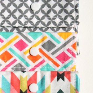 May include: Four fabric pouches with different geometric patterns. Each pouch has a white snap closure. The pouches are stacked on top of each other.