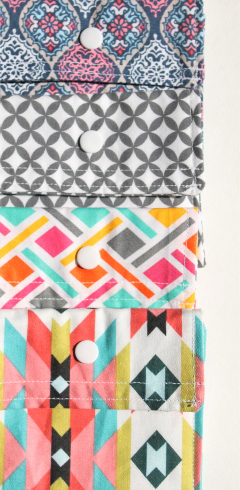 May include: Four fabric pouches with different geometric patterns. Each pouch has a white snap closure. The pouches are stacked on top of each other.
