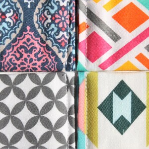 May include: Four fabric swatches with different geometric patterns. The top left swatch has a blue, pink, and white paisley pattern. The top right swatch has a white background with pink, orange, and gray geometric shapes. The bottom left swatch has a white background with gray circles. The bottom right swatch has a white background with a teal, pink, yellow, and gray geometric pattern.