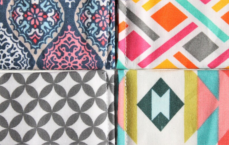 May include: Four fabric swatches with different geometric patterns. The top left swatch has a blue, pink, and white paisley pattern. The top right swatch has a white background with pink, orange, and gray geometric shapes. The bottom left swatch has a white background with gray circles. The bottom right swatch has a white background with a teal, pink, yellow, and gray geometric pattern.