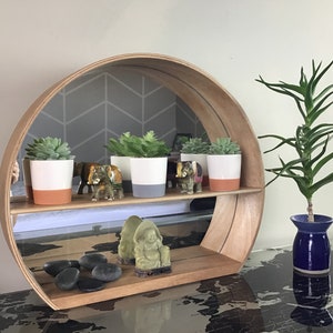 May include: A round wooden shelf with a mirror in the back. The shelf has two tiers and is decorated with small potted succulents, miniature elephants, and a small green Buddha statue. The shelf is sitting on a table with a world map design.