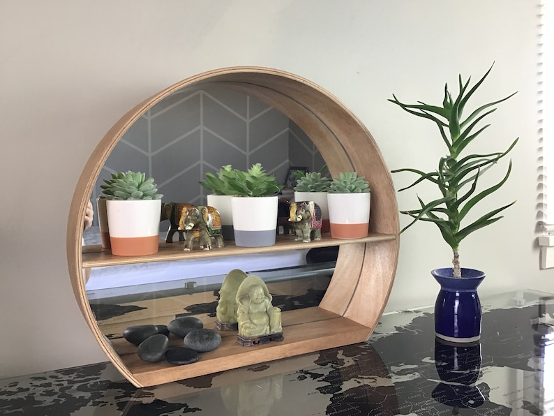 May include: A round wooden shelf with a mirror in the back. The shelf has two tiers and is decorated with small potted succulents, miniature elephants, and a small green Buddha statue. The shelf is sitting on a table with a world map design.