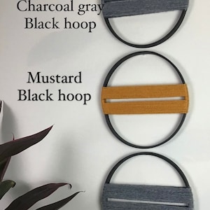 Puede incluir: Tres decoraciones de pared circulares. Cada una tiene un aro de metal negro con una banda de hilo. Los aros superior e inferior tienen hilo gris carbón, mientras que el aro central tiene hilo color mostaza. El texto en la pared dice "Charcoal gray Black hoop" y "Mustard Black hoop."