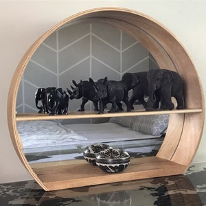 May include: A circular wooden shelf with two tiers. The top tier has a mirrored backing and features black rhino and elephant figurines. The bottom tier has two black and white decorative bowls.