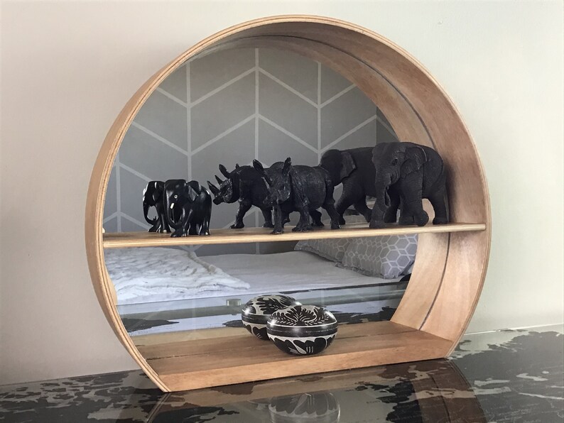 May include: A circular wooden shelf with two tiers. The top tier has a mirrored backing and features black rhino and elephant figurines. The bottom tier has two black and white decorative bowls.
