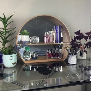 May include: A round wooden shelf with a mirrored back, displaying various bottles of cosmetics and nail polish. The shelf is on a glass table with a world map design. There are two potted plants on the table, one with green leaves and the other with purple leaves.