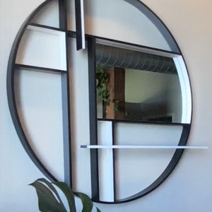 May include: A black and white circular wall shelf with geometric shapes and a mirror in the center. The shelf is mounted on a white wall.