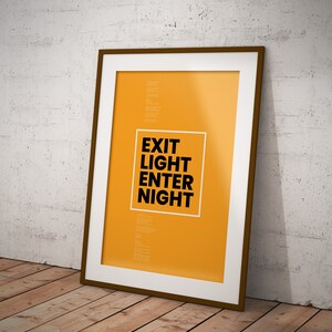 Op de afbeelding: Een ingelijste poster met een gele achtergrond en zwarte tekst die "EXIT LIGHT ENTER NIGHT" luidt.