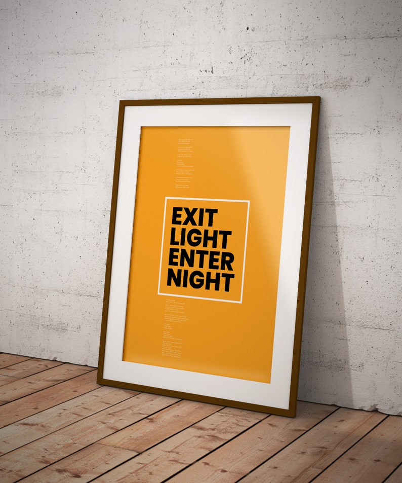 Op de afbeelding: Een ingelijste poster met een gele achtergrond en zwarte tekst die "EXIT LIGHT ENTER NIGHT" luidt.