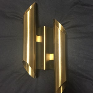 May include: A gold-toned wall sconce with three cylindrical light fixtures. The fixtures are angled and arranged in a staggered pattern.