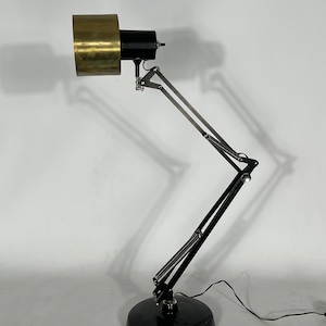 May include: A black and silver adjustable desk lamp with a brass shade. The lamp has a long, flexible arm and a round base.