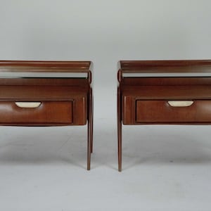 May include: Two matching wooden nightstands with a warm brown finish. Each has a drawer with a light-colored handle and a glass top shelf. The nightstands have slender, tapered legs.