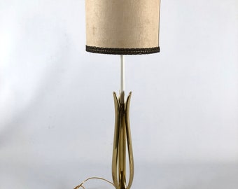 May include: A gold table lamp with a white marble base and a beige lampshade with a brown trim. The lamp has a unique, stylized design that resembles a flower.
