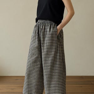 May include: A person wearing a black sleeveless top and wide-leg, black and white checkered pants. The person is also wearing black flats. The outfit is casual and comfortable, suitable for everyday wear.