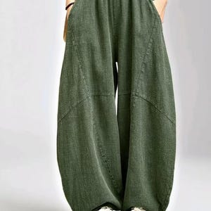 以下が含まれることがあります： オリーブグリーンのワイドパンツ。ハイウエストのゴム仕様で、深いサイドポケットとフロントの目立つ斜めの縫い目が特徴です。全体的にボリュームのあるゆったりとしたシルエットで、裾に向かってわずかに細くなっています。