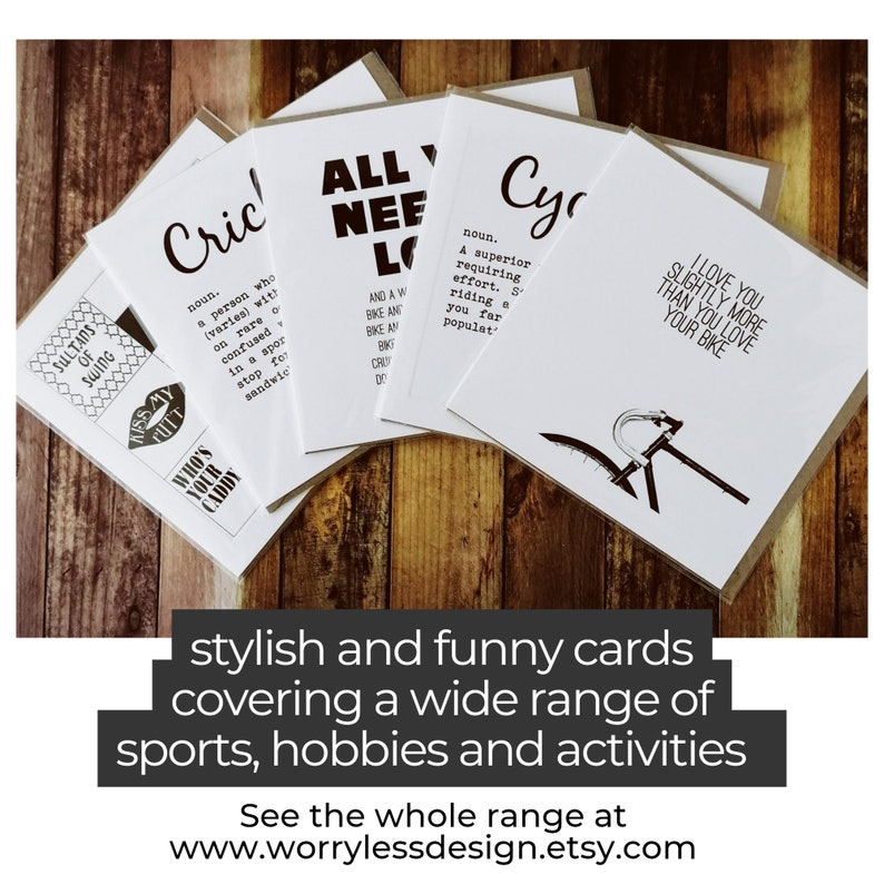 May include: A collection of white greeting cards with black text, featuring humorous definitions and phrases related to sports and hobbies. The cards are displayed on a wooden surface. Text on the cards includes "Cricket", "All You Need is Love", and "I Love You Slightly More Than You Love Your Bike".