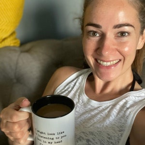 May include: White ceramic coffee mug with black rim and handle. The mug has black text that reads "I might look like I'm listening to you but in my head I'm running."