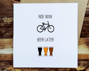 May include: White greeting card with the text "RIDE NOW BEER LATER" above a black bicycle illustration and three beer glasses. The card is on a brown envelope, with a wooden background.