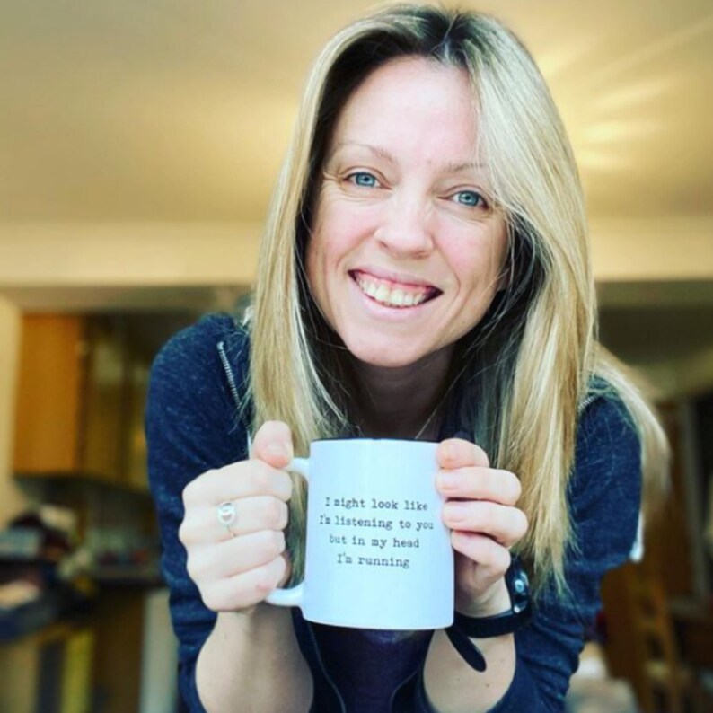 May include: A white ceramic mug with a black rim and handle. The mug has black text that reads "I might look like I'm listening to you but in my head I'm running". A person is holding the mug with both hands.